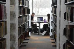 female student and male student studying at table in library between bookstacks